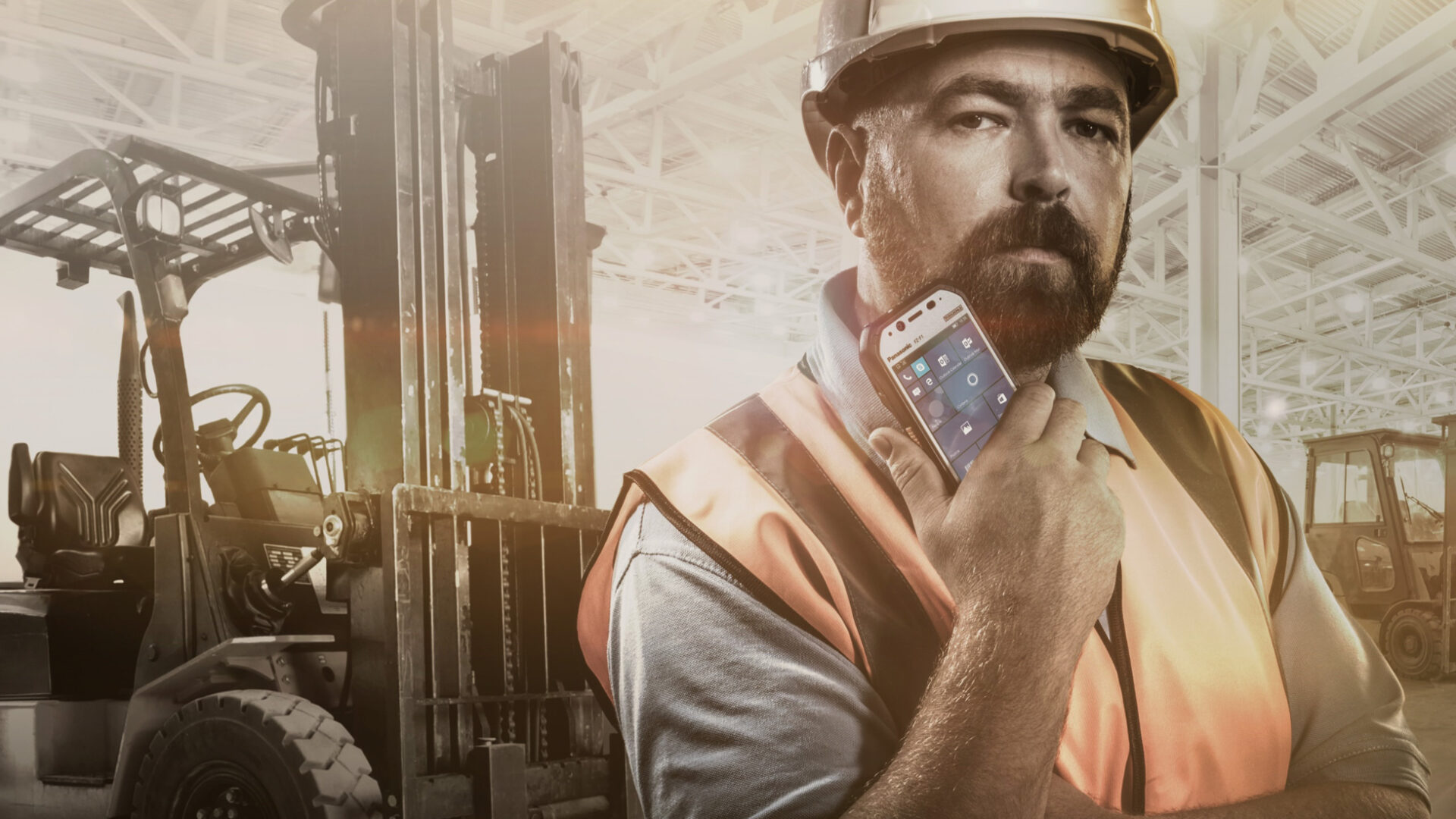 Industriemitarbeiter vor Gabelstapler in Lagerumgebung hält ein mobiles Terminal mit mobiler Software-Lösung für digitale Logistikprozesse
