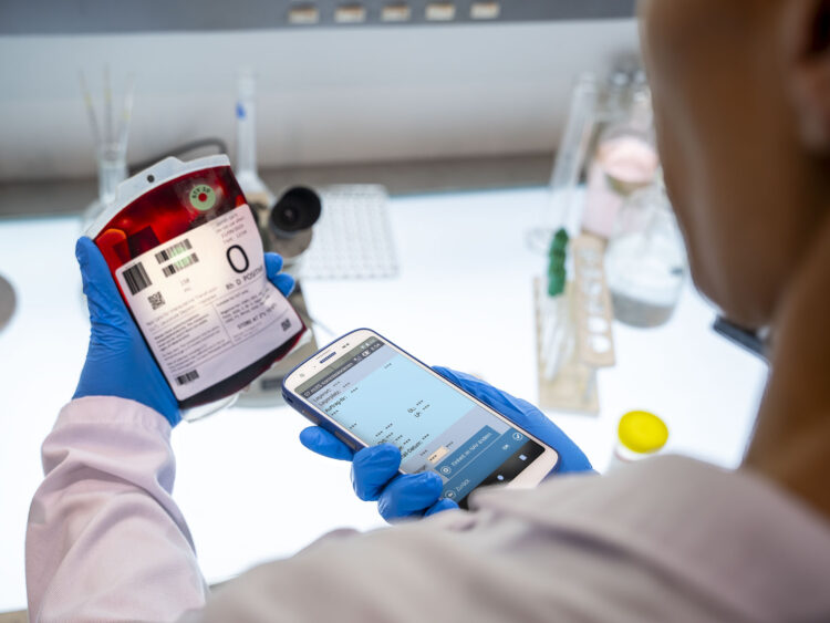 Employée de laboratoire scanne une poche de sang avec un ordinateur mobile pour une traçabilité sûre
