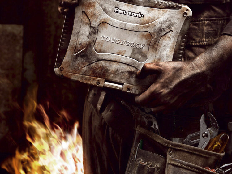 Arbeiter hält ein Rugged Notebook der Marke Panasonic Toughbook in staubiger Industrieumgebung mit Feuer im Hintergrund