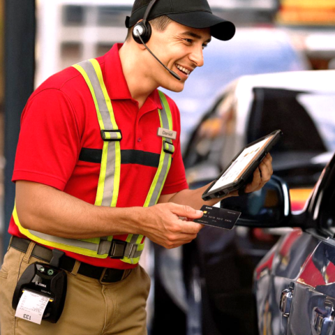 Un employé d'une agence de location de voitures utilise une tablette d'entreprise Zebra ET401, une imprimante mobile de reçus et un casque audio pour saisir des données et effectuer un paiement directement sur place