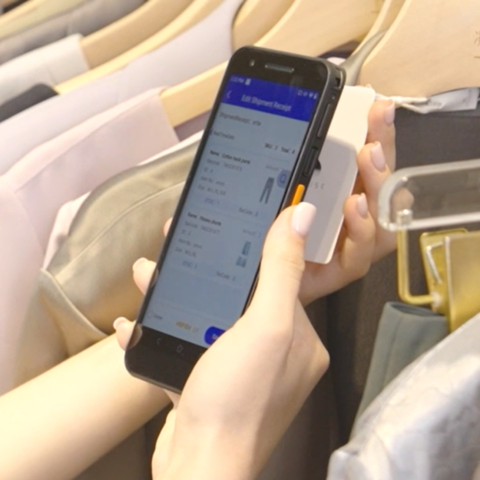Une employée scanne une étiquette RFID à l'aide d'un ordinateur mobile RFID Urovo DT610, au design fin semblable à celui d'un smartphone, dans un magasin de vêtements