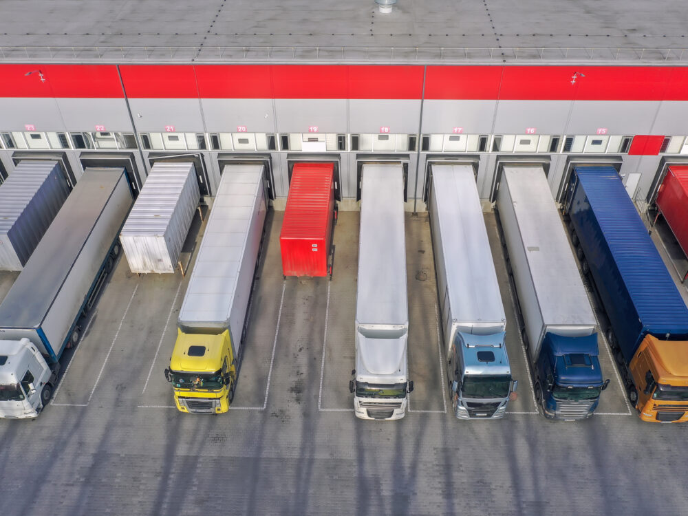 Drohnenaufnahme eines Logistikzentrums mit LKWs an Laderampen illustriert die Kapazitätsplanung und das Flottenmanagement mit der Software-Lösung Tourenplanung von mobit