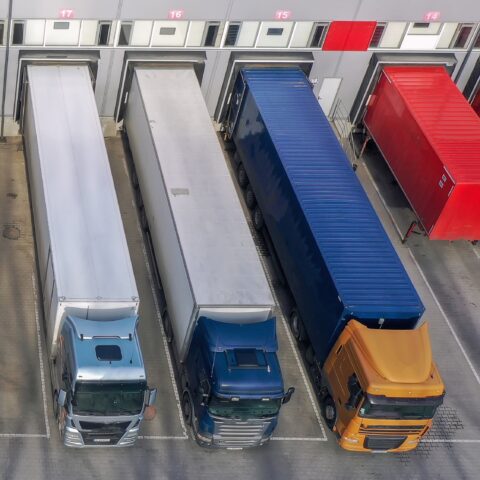 Article de blog de mobit sur PTV Logistics et OptiFlow - vue aérienne d'un centre logistique avec des camions sur les quais de chargement illustre la planification des capacités et la gestion de flotte avec la solution logicielle de planification d'itinéraires de mobit