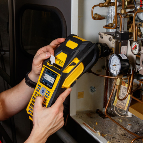 Wartungsmitarbeiter druckt Etiketten mit einem Brady M610 Handheld-Labelprinter zur Kennzeichnung von Rohrleitungen in einer industriellen Installation